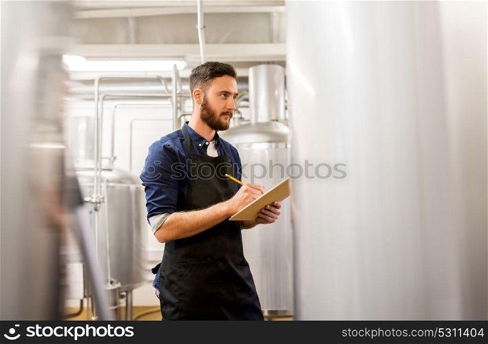 manufacture, business and people concept - man with clipboard working at craft brewery or beer plant. man with clipboard at craft brewery or beer plant