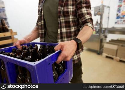 manufacture, business and people concept - man with glass bottles in box at craft brewery or non-alcoholic beer production plant. man with bottles in box at craft beer brewery
