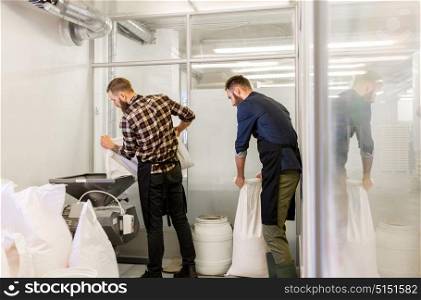 manufacture, business and people concept - men with bags weighing and pouring malt to mill at craft brewery or beer plant. men with malt bags and mill at craft beer brewery