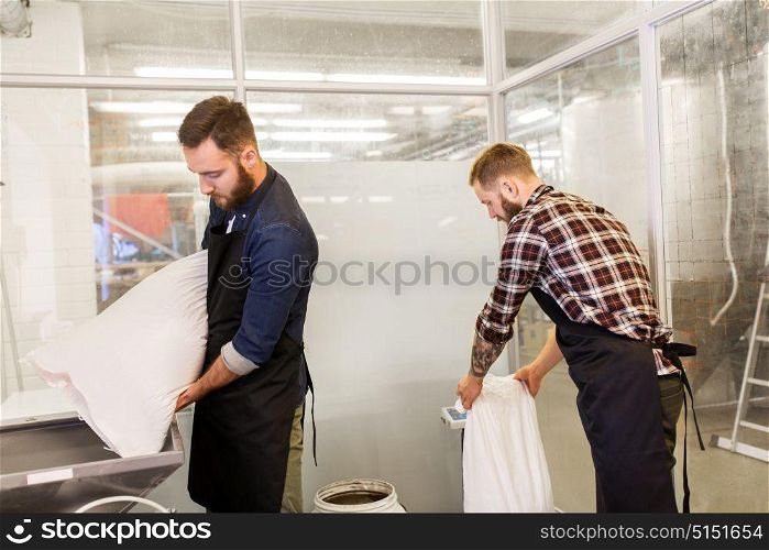 manufacture, business and people concept - men with bags weighing and pouring malt to mill at craft brewery or beer plant. men with malt bags and mill at craft beer brewery