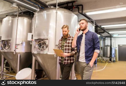 manufacture, business and people concept - men with clipboard working at craft brewery or beer plant and calling on smartphone. men working at craft brewery or beer plant