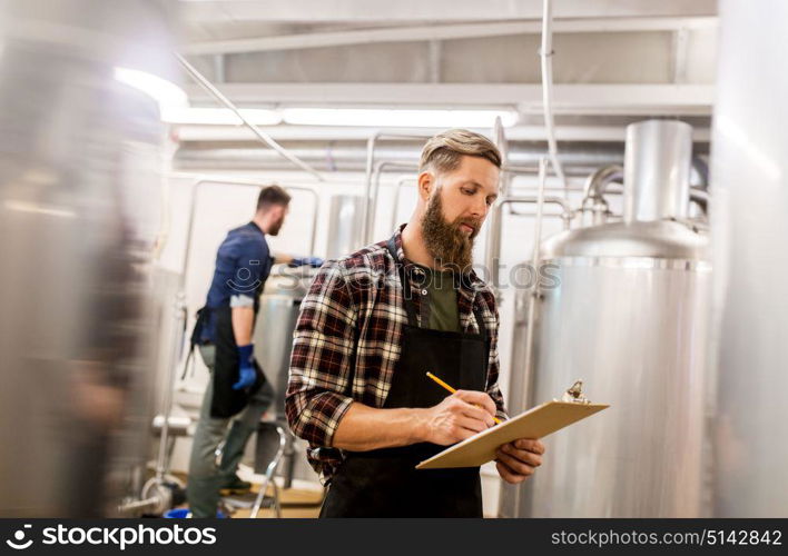 manufacture, business and people concept - men with clipboard working at craft brewery or beer plant. men with clipboard at craft brewery or beer plant