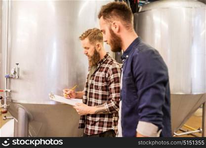 manufacture, business and people concept - men with clipboard working at craft brewery or beer plant. men with clipboard at craft brewery or beer plant