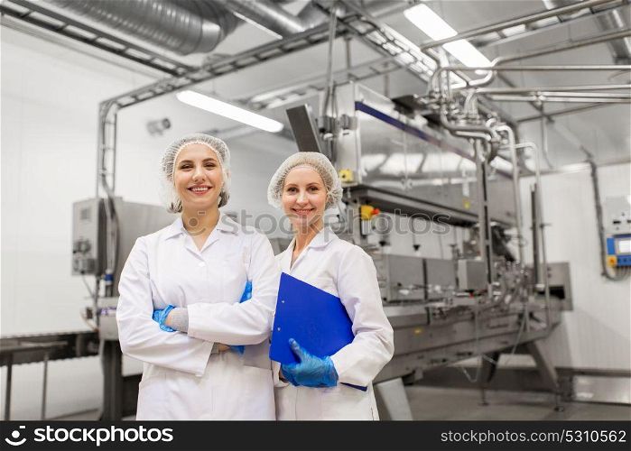 manufacture, industry and people concept - happy women technologists with clipboard at ice cream factory shop. happy women technologists at ice cream factory