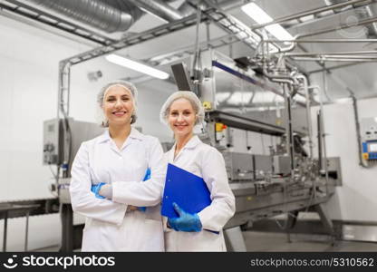 manufacture, industry and people concept - happy women technologists with clipboard at ice cream factory shop. happy women technologists at ice cream factory