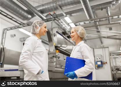 manufacture, industry and people concept - happy women technologists with clipboard at ice cream factory shop. happy women technologists at ice cream factory