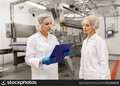manufacture, industry and people concept - women technologists with clipboard at ice cream factory shop. women technologists at ice cream factory