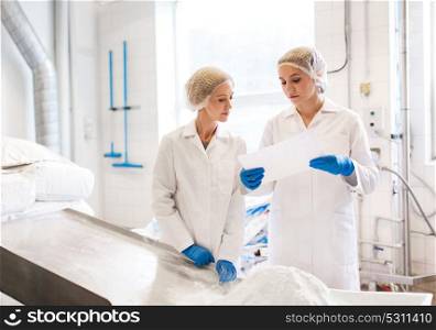 manufacture, industry, food production and people concept - women technologists with paper and powdered milk at ice cream factory shop. women technologists working at ice cream factory