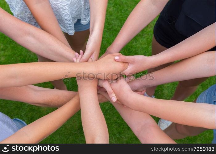 Many arms of girls holding hands together above green grass
