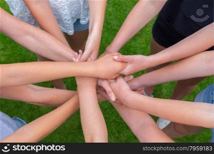Many arms of girls holding hands together above green grass