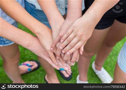 Many arms of girls with hands on top of each other above green grass