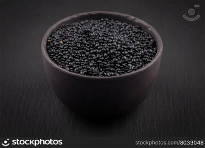 many black beluga lentil seeds in small dark bowl cup isolated on white