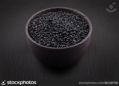 many black beluga lentil seeds in small dark bowl cup isolated on white