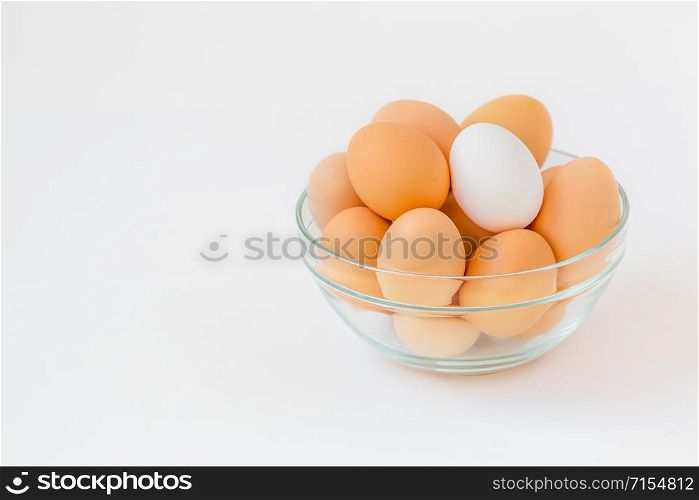 Many brown eggs with one white egg in a glass bowl. While cooking in the kitchen ingredients.. Many brown eggs with one white egg in a glass bowl.