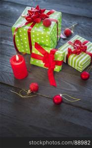 Many cheerful gifts, wrapped in green paper and tied with red ribbons and bows, surrounded by Xmas decorations, and a lit candle, on a vintage wooden table.
