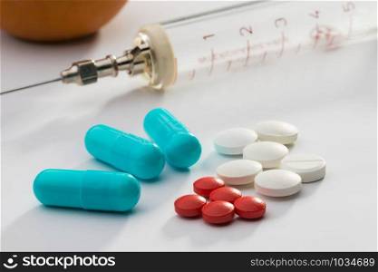 Many colored pills, tablets and capsuls for pharmacy and medicine, with a syringe