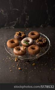 Many different donuts on glass plate on dark stone background