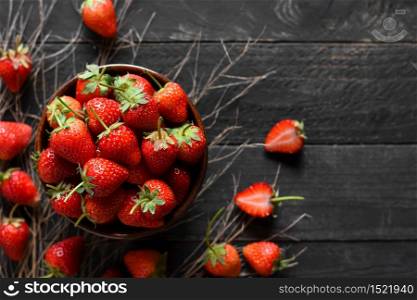 Many fresh strawberries are put in a bowl and placed on a black wooden table.