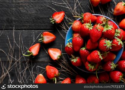 Many fresh strawberries are put in a bowl and placed on a black wooden table.