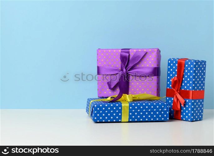 many gift boxes tied with a silk ribbon on a white wooden table, blue background. Festive backdrop, copy space