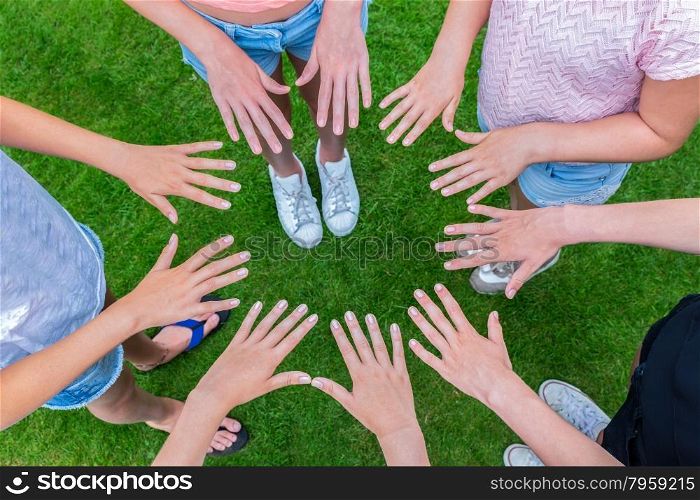 Many hands of young girls making circle above green grass