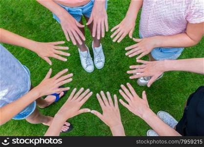 Many hands of young girls making circle above green grass