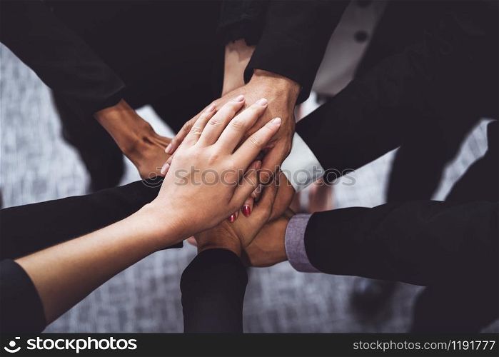 Many happy business people stacking hands together with joy and success. Company employee celebrate after finishing successful work project. Corporate partnership and achievement concept.