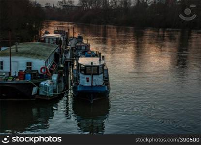 many House boats are beached on the side of the River Thames at sunset