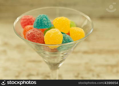 Many jellybeans close up in glass jar with differents colors on wooden background