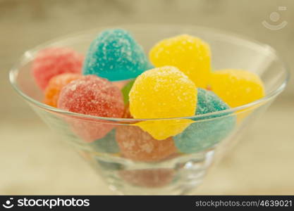 Many jellybeans close up in glass jar with differents colors on wooden background