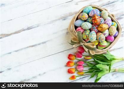 Many mixed colorful painted eggs on basket and tulips on white wood table. Easter background concept.