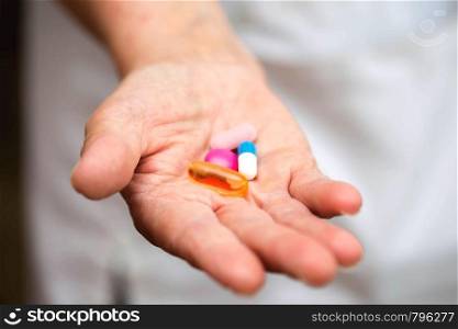 Many multi-colored pills in a Senior's hands. Painful old age. Caring for the health of the elderly nurse. Many multi-colored pills in a Senior's hands. Painful old age. Caring for the health of the elderly