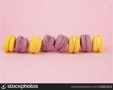 many multi-colored round baked macarons cakes on a light pink background, top view