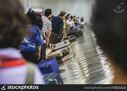 Many passengers waiting suitcase or luggage with circulating conveyor belt in the international airport.