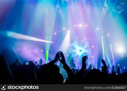 Many people enjoying concert, band performs on stage in the bright blue light, people enjoying music, dancing with raised up hands and clapping, active night life
