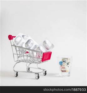 many pills small glass with shopping cart with silver blister pills white background . Resolution and high quality beautiful photo. many pills small glass with shopping cart with silver blister pills white background . High quality and resolution beautiful photo concept