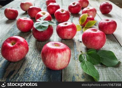Many red apples with green leaves lie on the old wooden table