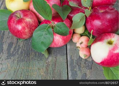 Many red apples with green leaves on the old wooden table