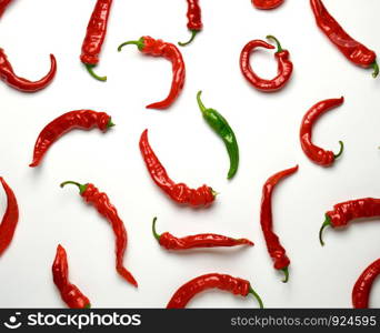 many red whole fruits of hot pepper and one green on a white background, concept of difference and discrimination