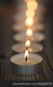 Many small burning candles in line on a wooden surface
