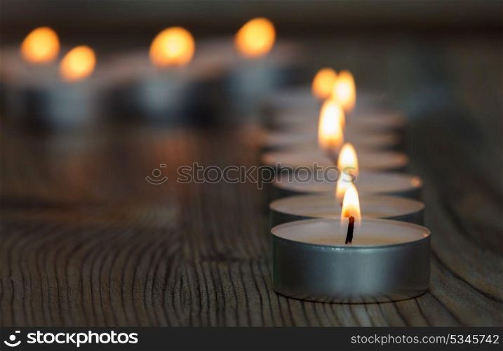 Many small burning candles on a wooden surface