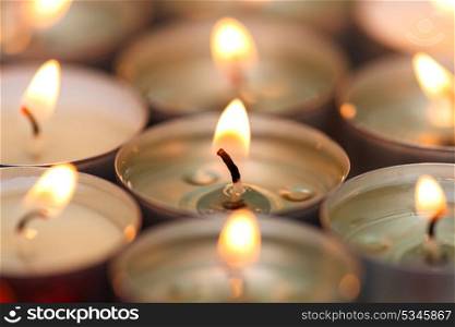Many small burning candles on a wooden surface