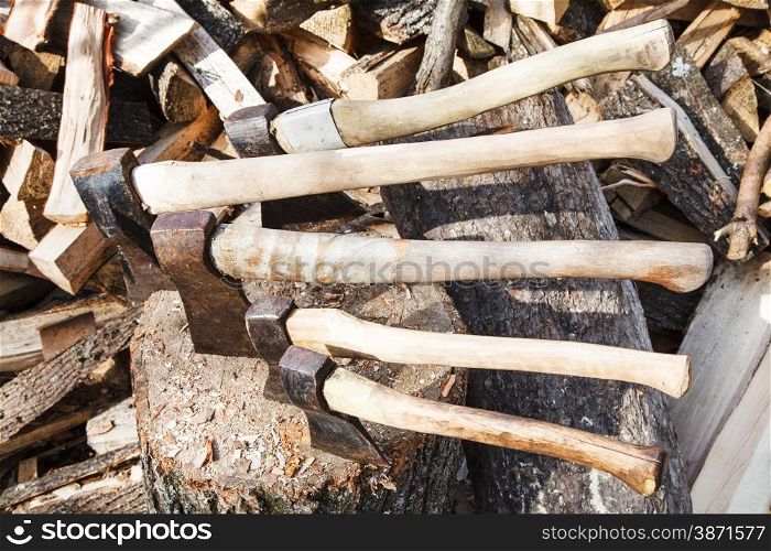 many various axes in wood block near stack of firewoods