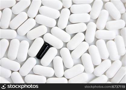 many white pills with one black pill in a middle