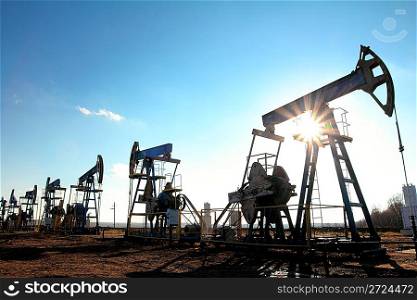 many working oil pumps silhouette in row against sun