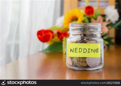 Many world coins in a money jar with wedding label on jar, beautiful flowers on background