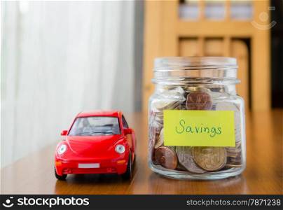 Many world coins in money jar with savings label on jar and a red car model, concept to financial planning for car loan