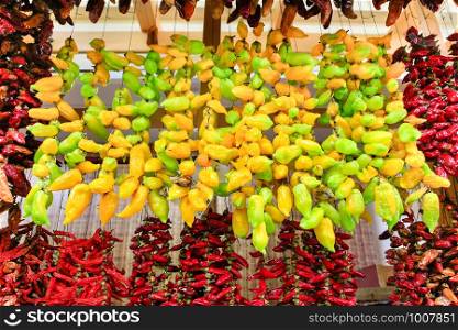Many yellow and red chilli peppers hang at ropes on market in Portugal