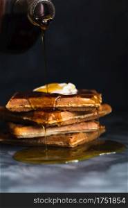 Maple syrup pouring onto a pile of waffles topped with butter