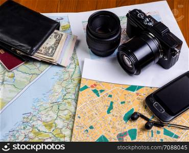 Maps on the table, a black camera with lenses and a smartphone with headphones. Planning a trip. Maps, money, smartphone and camera
